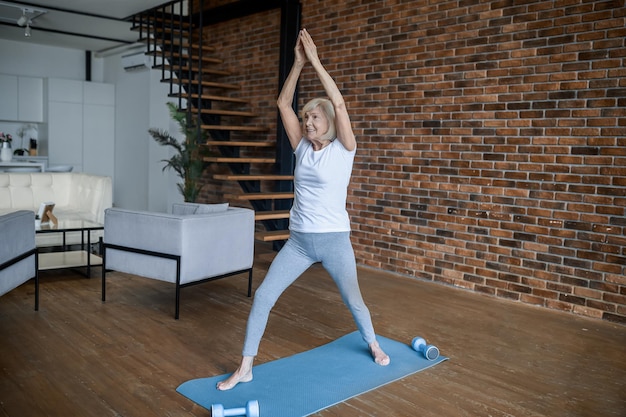 Training. Grijsharige senior vrouw staat met haar armen omhoog