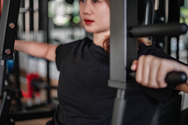 Training gym concept a female teenager using a gym equipment pulling her arms against the machine.