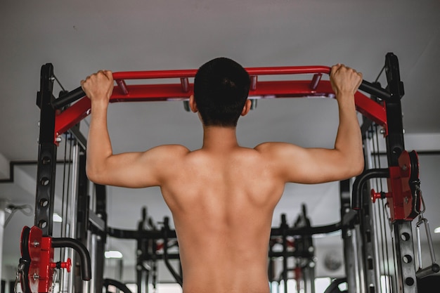 Концепция тренажерного зала тренировки сильного молодого человека, использующего обе руки, делая подтягивания; подтягиваясь вверх и вниз на тренажерах.