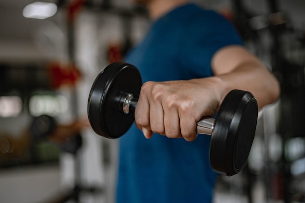 Training gym concept a young adult using his muscular strong arm lifting a dumbbell upward and downward in the gym.