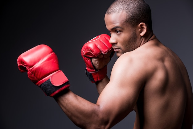 Allenare le sue abilità di boxe. vista laterale del giovane africano senza camicia in guantoni da boxe che si esercita