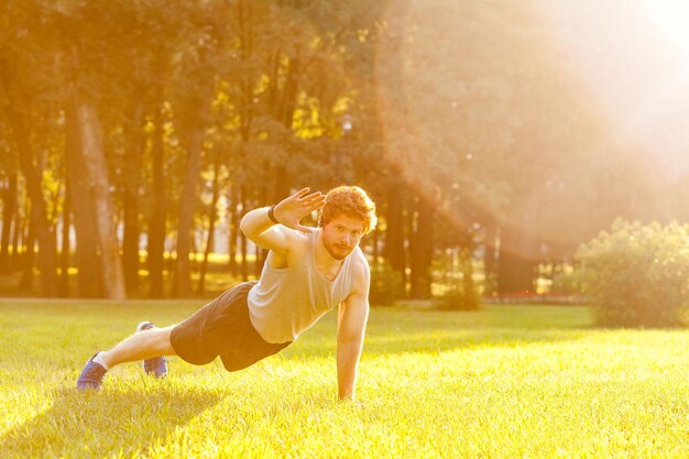 Training in one summer morning young adult bearded man looking in camera and doing exercise