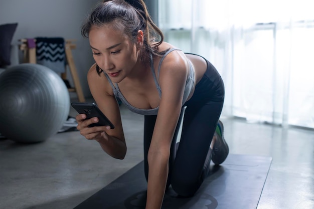 Training thuis concept Sportieve Aziatische vrouw die oefening doet tijdens het kijken naar online tutorial op smartphone jonge vrouw die traint in de woonkamer en naar mobiele telefoon kijkt