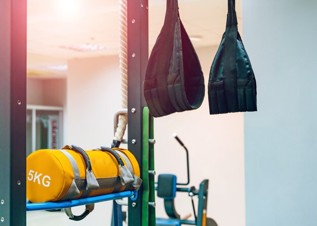 Trainingsriemen trx hangen aan de muur en ponsen gele tas met 5 kg in de sportschool.