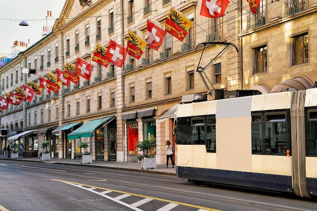 Tram in Rue de la Corraterie Street with Swiss flags in the center of Geneva, Switzerland. People on the background