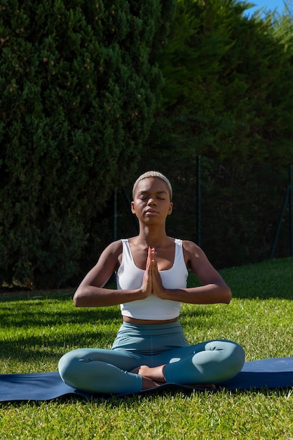 Tranquil black woman with short hair sitting in Lotus pose with prayer hands and closed eyes