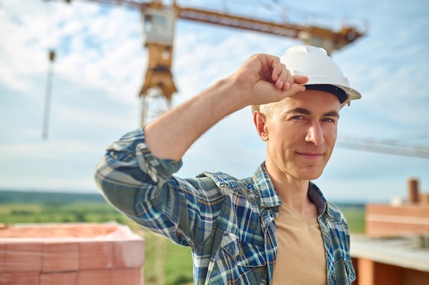 Tranquil foreman in a hardhat standing among stacked red bricks