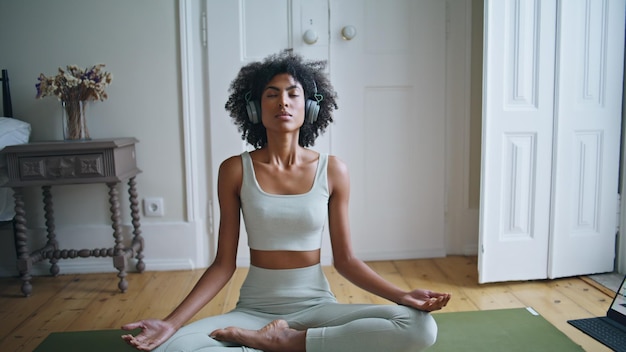 Tranquil lady meditating on carpet zoom out african woman sitting lotus pose