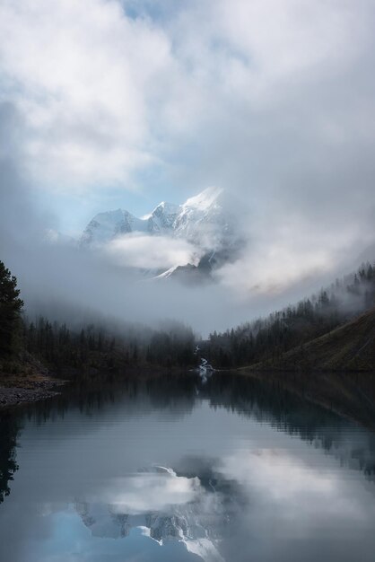 写真 雲の中の雪の城の静かな風景 山の小川は森の丘から氷河の湖に流れます 霧の清潔な雪の山は小さな川と針葉の木が静かなアルプスの湖に反映されています