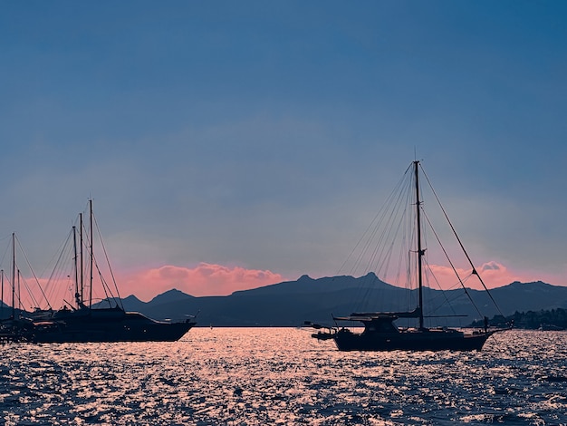 静かな海の景色と沿岸の自然の概念は、日没時に地平線上の山と青い空をボートします