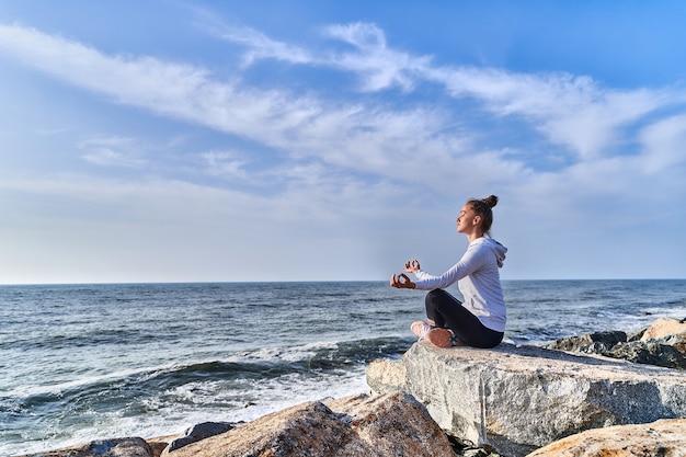 Photo tranquil woman in lotus position meditates and relaxes on a cliff