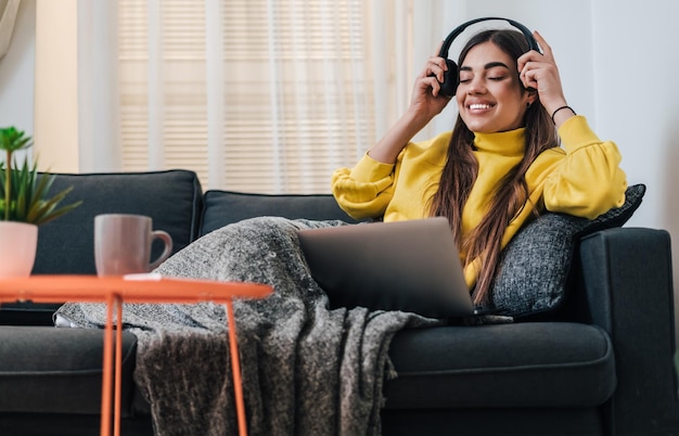 Tranquil young caucasian girl watching show on laptop putting headphones on