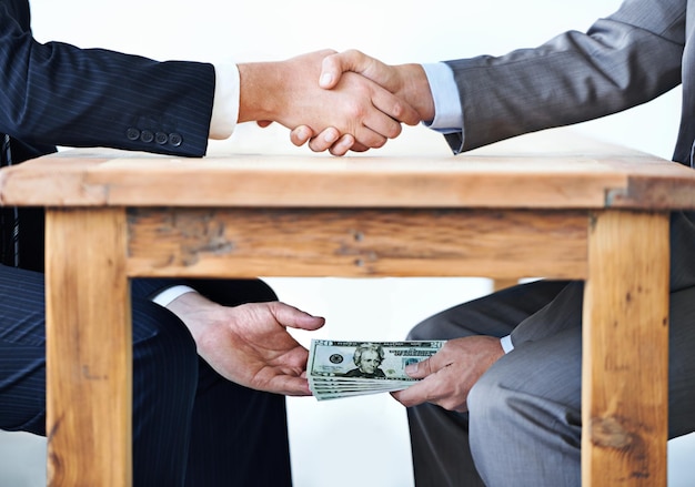 Foto transacties onder de tafel bijgesneden opname van twee zakenlieden die elkaar de hand schudden terwijl geld onder een tafel de handen doorgeeft