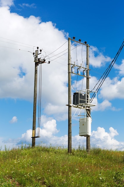 Трансформаторы электрического поста с кабелями линий электропередач против яркого голубого неба. Трансформатор с полюсами электричества в поле.