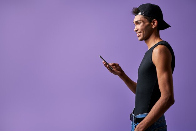 Transgender smiling male with mobile in hand side view on purple background portrait