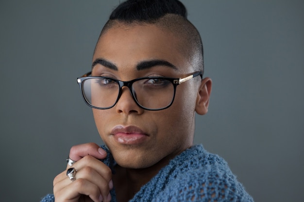 Трансгендерная женщина в очках над серой стеной