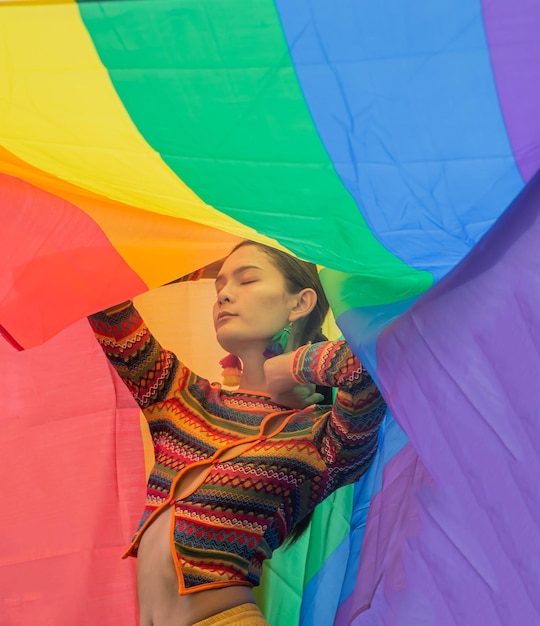 Transgender woman wearing a rainbow dress and a rainbow flag background poses confidently and proudly of her genderlgbtq lifestyle conceptlgbtq pride month