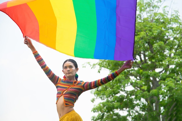 Transgendervrouw die een regenboogjurk draagt en een regenboogvlag vasthoudt, poseert vol vertrouwen en trots voor haar genderlbtq-levensstijlconceptlgbtq pride-maand
