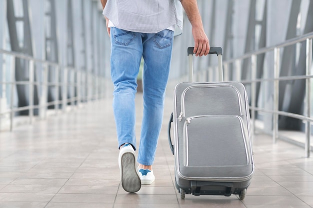 Концепция транзитного пассажира Неузнаваемый человек, идущий с чемоданом в терминале аэропорта