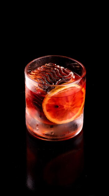 Translucent crystalline ice decorated big wavy for a glass of negroni drink on black table isolated