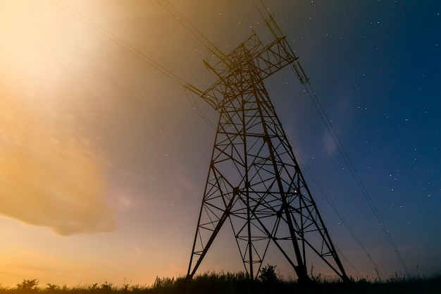 Transmission and long distance distribution of electricity concept. Angled view of high voltage tower with electric power lines stretching on dark blue starry sky.