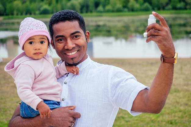 国境を越えた異人種間の父親は、秋の公園で彼の混血の女の赤ちゃんの吸入喘息吸入器に与えます。