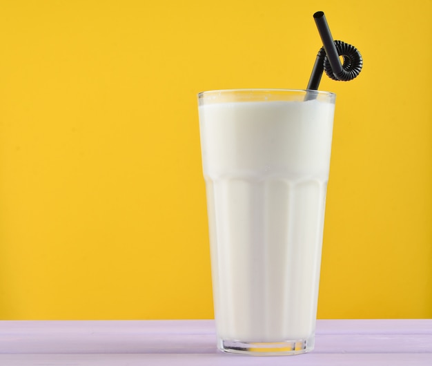 Transparant glas met verse biologische melk, cocktail buisjes op een pastelkleur houten tafel geïsoleerd op een geel. kopieer ruimte