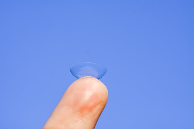 Transparante contactlens op vingertop op de wazige groene achtergrond van de zomeraard.