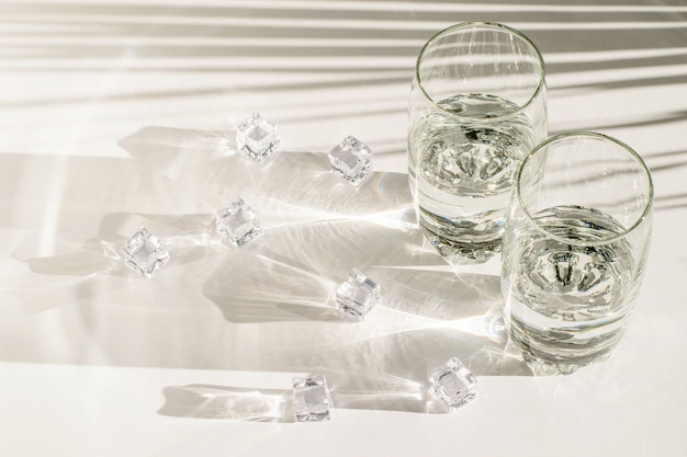 Transparante glazen en stukjes ijs op wit
