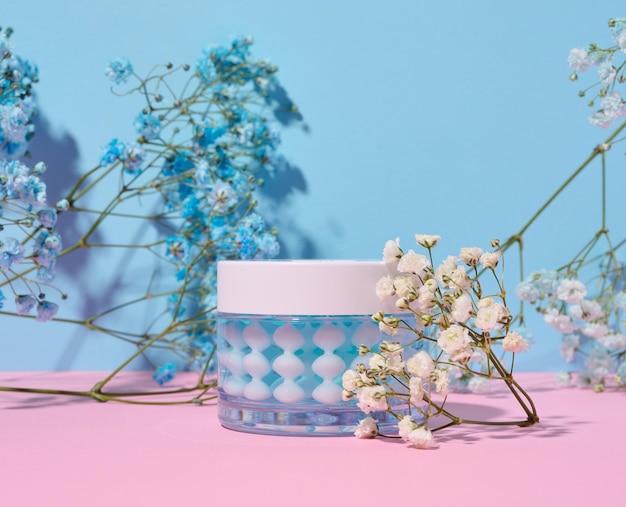 Transparante glazen pot met gezichtscrème op een roze blauwe achtergrond cosmetica