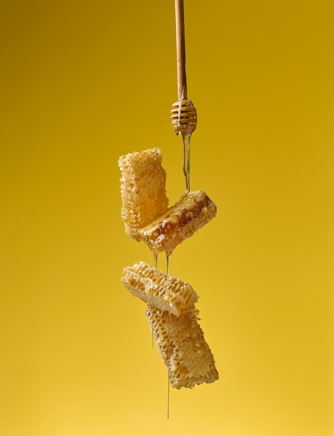 Transparante zoete honing uit een houten stok op een was honingraat gele achtergrond voedsel
