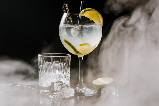 Transparent alcohol cocktail with lime and ice on the smoky background