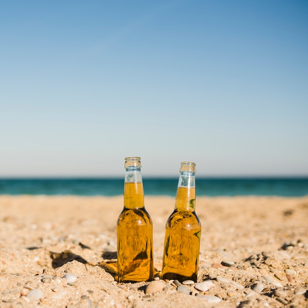 Transparent beer bottles in the sand at beach against clear sky