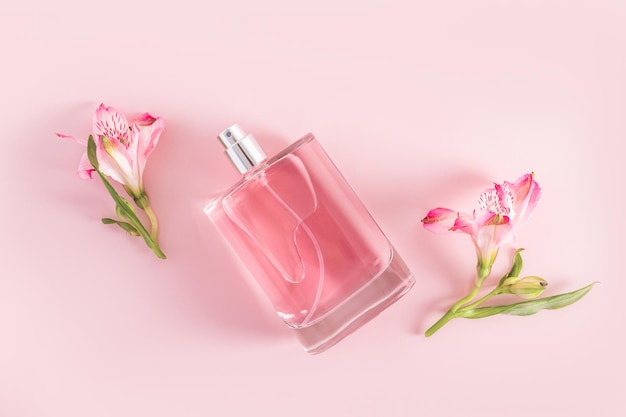 A transparent bottle of cosmetic product eau de parfum or spray closeup on a pink background with buds of spring flowers product advertising