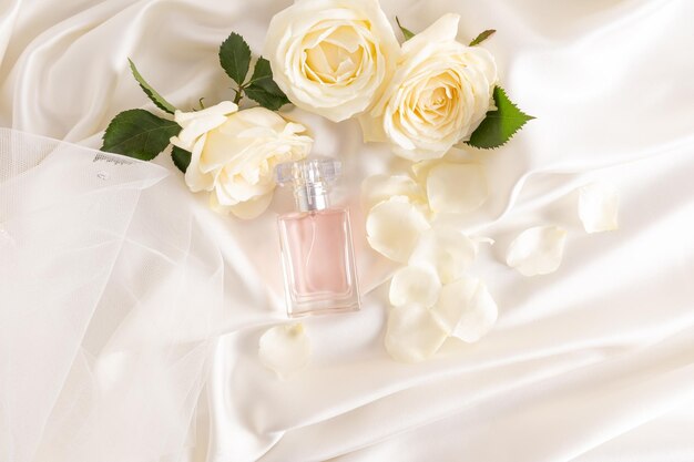 A transparent bottle of feminine among roses and delicate petals Satin fabric background in the color of champagne The concept of beauty