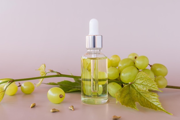 A transparent bottle with a pipette with natural cosmetic grape seed oil or whey against of ripe grapes vitamin E slowing down the aging process