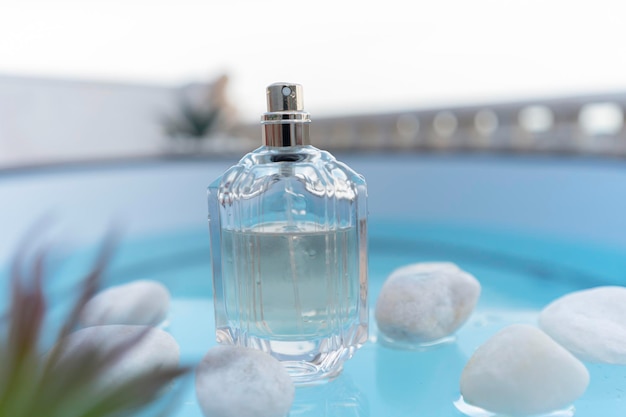 Transparent bottle with womens or mens perfume near white stones on the glass surface of the backgro