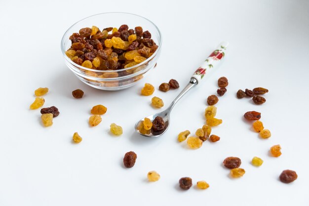 transparent bowl cup filled with multiple raisins isolated over the white background. Small dessert spoon with raisins. sultana. dry grapes