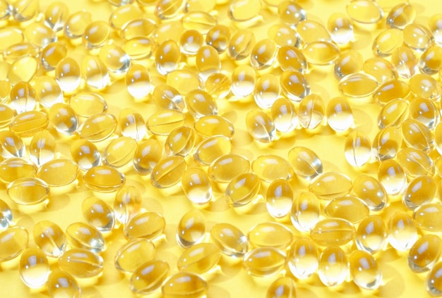 Прозрачные капсулы витамина D на желтом фоне крупным планом текстуры и фона