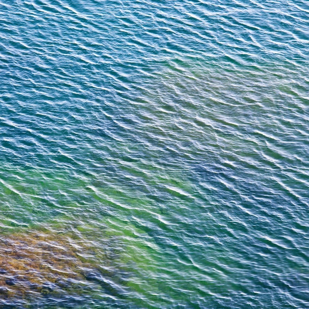 底にいくつかの石がある透明な沿岸の紺碧の水面