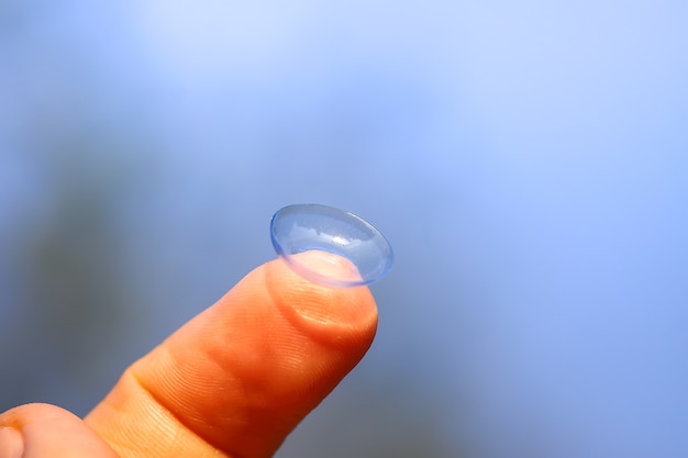 Transparent contact lens on finger tip on blurred green summer nature background.