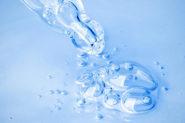Transparent cosmetic gel flows from an eyedropper directly onto the background in a large blob with bubbles On a blue background Hyaluronic acid toner toner gel cream Cosmetics