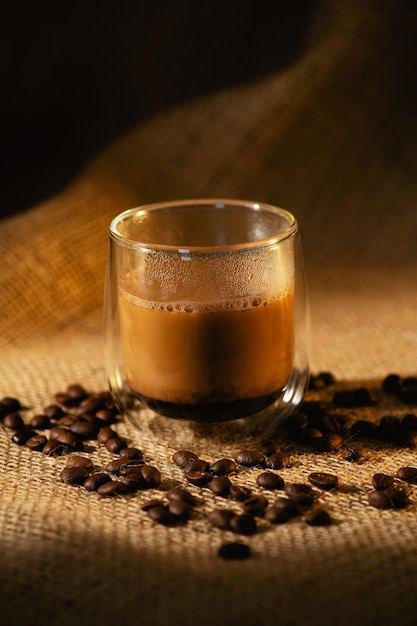 A transparent cup of coffee with milk on a dark burlap background