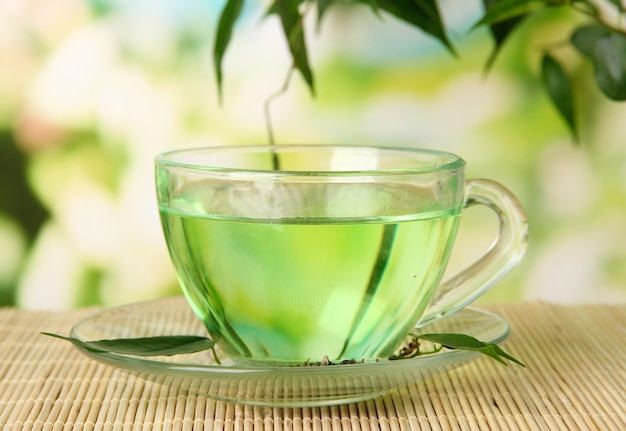 Transparent cup of green tea on bamboo mat on nature background