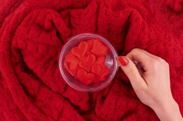 A transparent cup in the shape of a heart with red hearts is held by a woman's hand. Valentines day