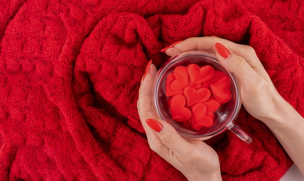 A transparent cup in the shape of a heart with red hearts is held by women's hands. Valentines day