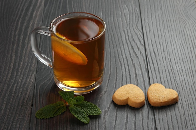 Transparent cup of tea with lemon, mint and cookies on a wooden table