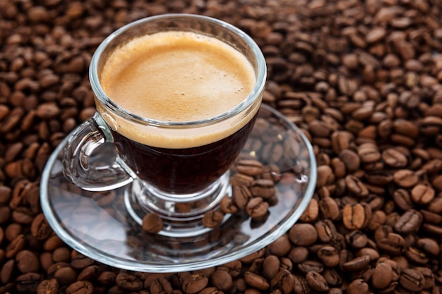 A transparent cup with aromatic frothy coffee stands on the beans. Close-up.