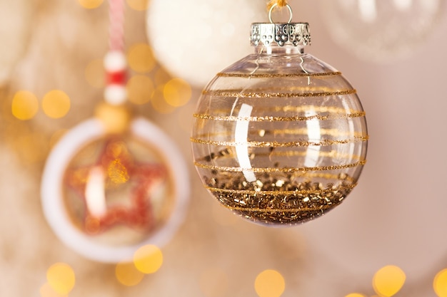 Transparent decorative ball with golden sparkling particles inside hanging in front of camera among other toys and decorations for Christmas tree