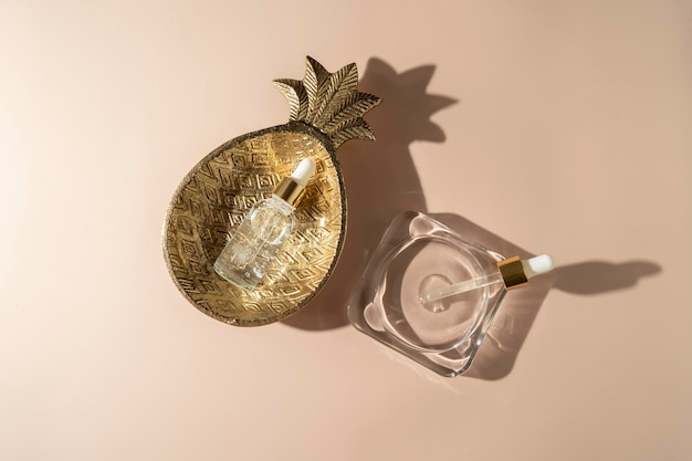 Прозрачная сыворотка для лица в бутылочке-капельнице или эфирное масло, лежащее на стеклянной и золотой тарелке на бежевом фоне
